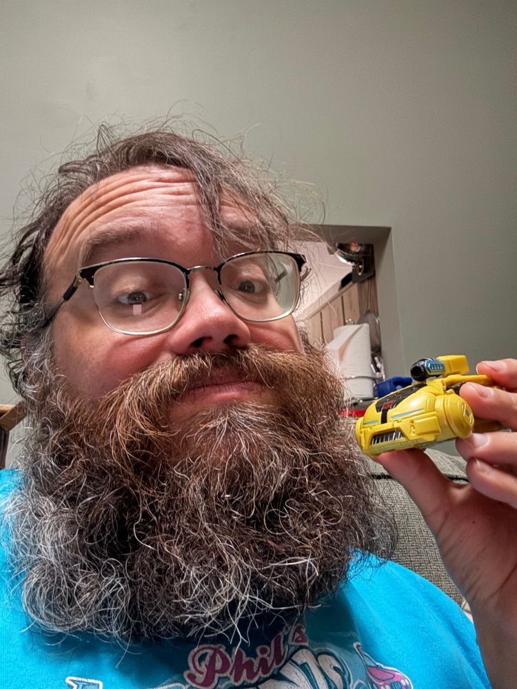 Bearded man with glasses, holding up Bumblebee in his Cybertron car mode.