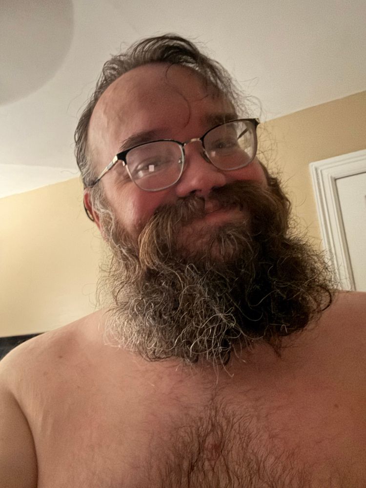 Bearded man with glasses, shirtless and smiling 