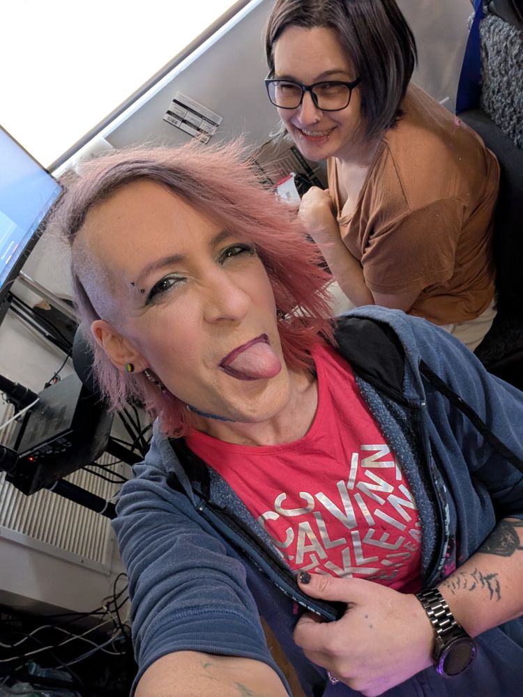 kaylee at her desk sticking her tongue out and getting jess to laugh too as she sits behind kaylee in her flight sim 🥰