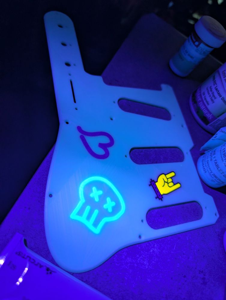 a 3d-printed pick guard for an electric guitar under a uv light, the inlaid graphics are uv reactive and glowing brightly