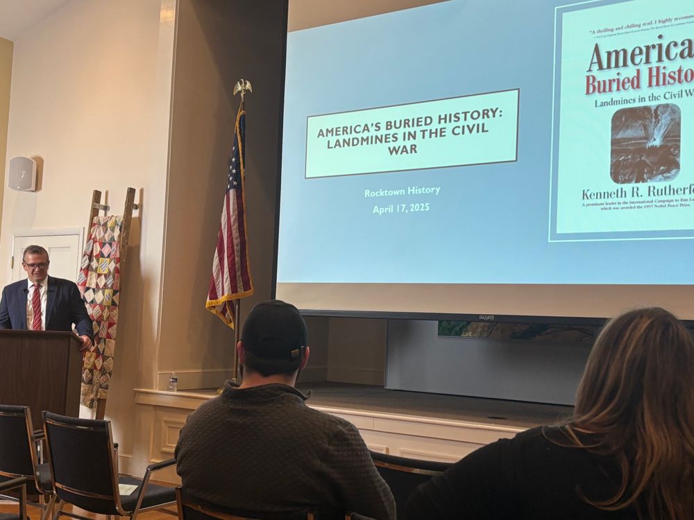 Dr. Ken Rutherford stands at a podium in front of the title slide of his presentation about landmines in the Civil War.
