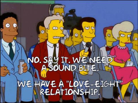 Screen grab from The Simpsons. An angry looking reporter, wearing a burgundy suit and holding a microphone, sits in a row with other members of the press, including a TV camera. The overlaid text is dialog from the scene: “No. Say it. We need a sound bite.” From off-screen Apu and his wife respond “We have a love-eight relationship.”