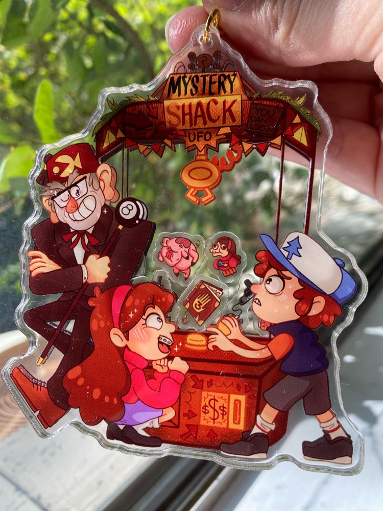 A keychain featuring Dipper, Mabel, and Stanley Pines playing at an arcade UFO claw machine game