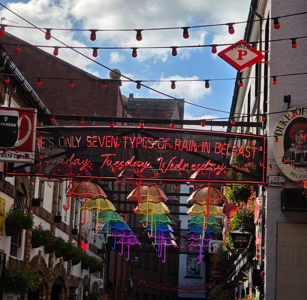 Additional shot of the colored umbrellas, with a sign saying "There's only seven types of rain in Belfast: Monday, Tuesday, Wednesday..."