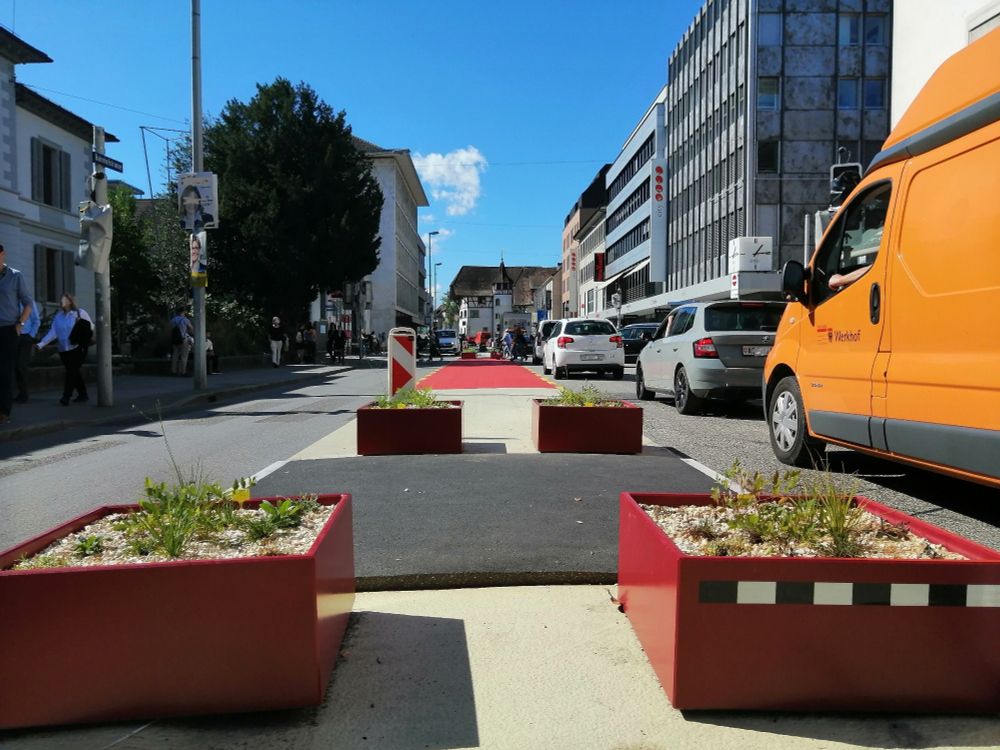 Street in the city of Aarau with three lanes. The middle lane is closed to automobiles, marked with different colors and decorated with flower pots.