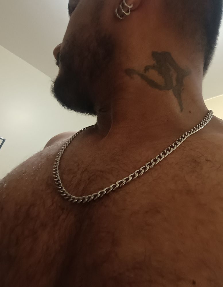 foto minha olhando pro lado, debaixo pra cima, na altura do peito, sem camisa, de corrente, brincos de argola e tatuagem no pescoço 