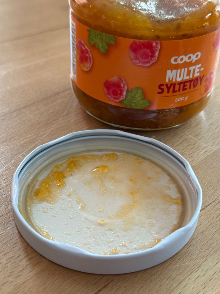 Ein geöffnetes Marmeladenglas, der Deckel liegt davor. Man erkennt, dass der Deckel einen inneren Teil (zum luftdichten Verschluss) und einen äußeren Ring (zum einfacheren Öffnen) hat