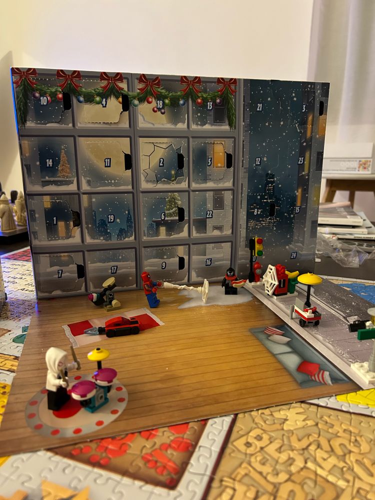 matty’s Lego Spider-Man advent calendar, opened to day 11. Spider-Gwen is playing the drums, Spider-man is webbing Venom who is eating a hot dog.