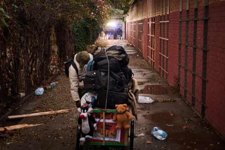 Una persona carica su un carrello i propri averi. In fondo alla via gli agenti di polizia controllano la situazione. 