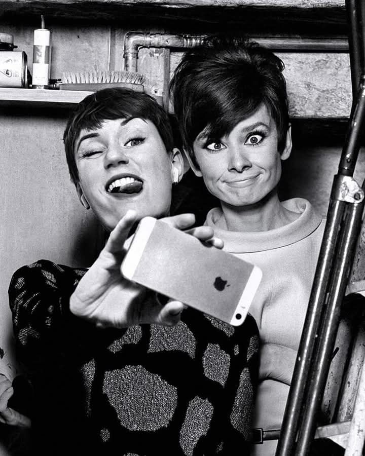 Due donne, in pose buffe, si scattano una fotografia. Si tratta di un fotomontaggio che vede la presenza della celebre attrice Audrey Hepburn.