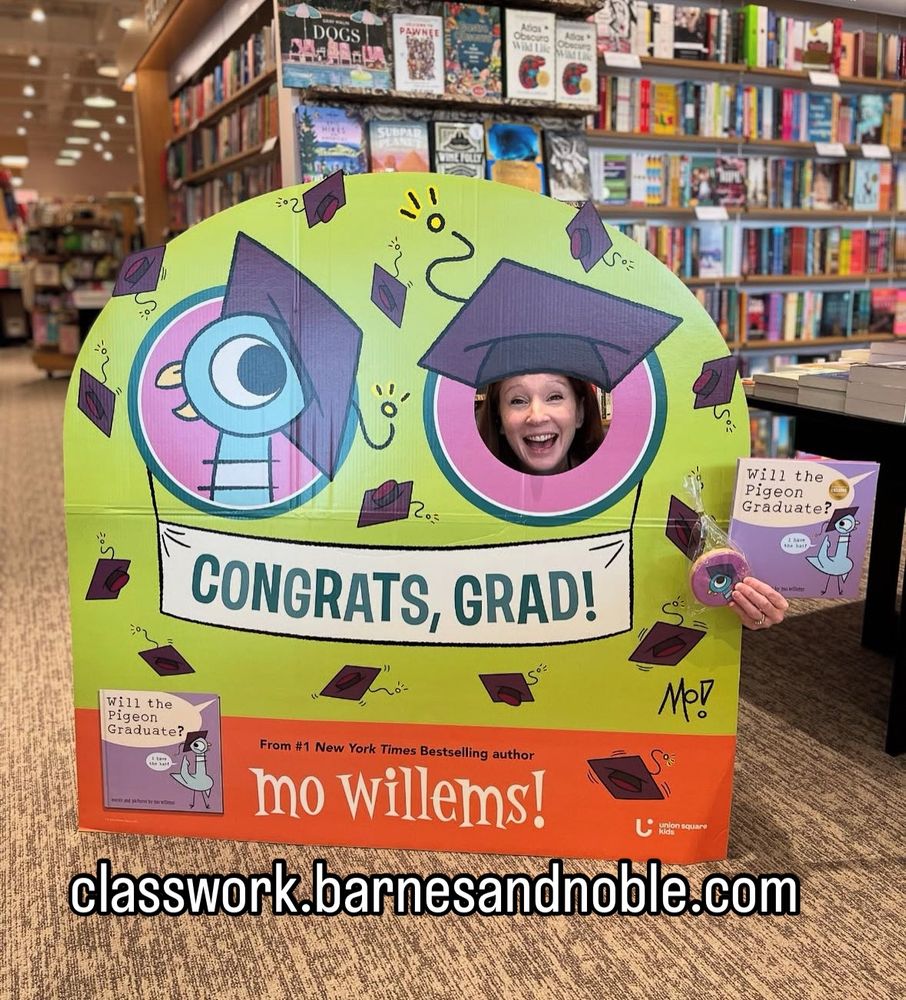The image shows a colorful Mo Willems’ Pigeon book display inside a Barnes & Noble store. The display is designed like a graduation-themed photo booth with a cutout hole where someone can put their face. The display features Pigeon (a beloved children’s book character) wearing a graduation cap, surrounded by flying caps and confetti. It says “Congrats, Grad!” in large letters.

A smiling woman, (the Wareham Store Manager), poses with her face in the cutout hole, appearing as part of the Pigeon-themed display. She holds a copy of “Will the Pigeon Graduate?”, the latest book in Mo Willems’ series, along with a Pigeon-themed cookie in her other hand.

In the background, bookshelves filled with colorful books line the store. At the bottom of the display, the website classwork.barnesandnoble.com is prominently featured, encouraging educators to explore ordering options for schools and classrooms.