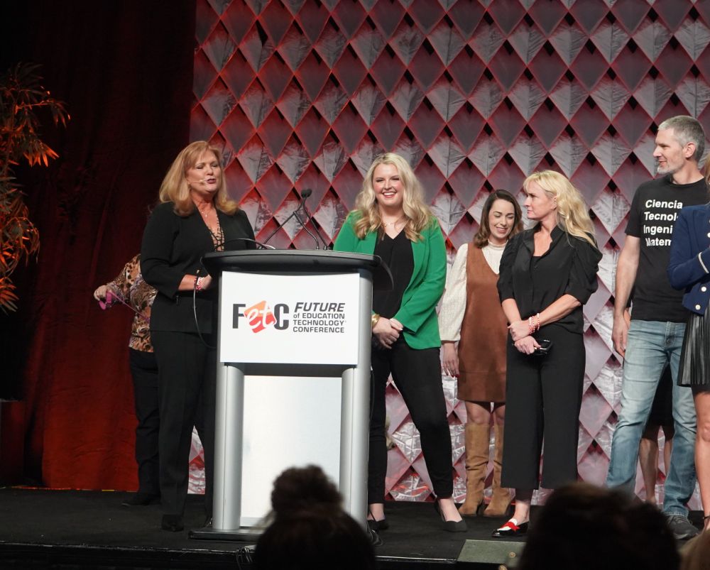 A blonde woman standing at a podium on stage at FETC