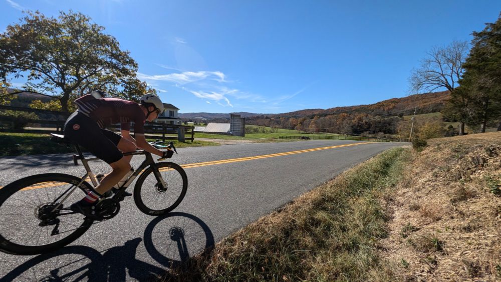 Road cyclist coming into frame from the left and going down a hill surrounded by trees and farms