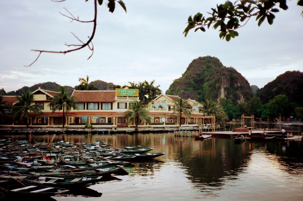 Photo du lac de Tam Coc, on y voit des dizaines de barques attachées au rivage et un hôtel