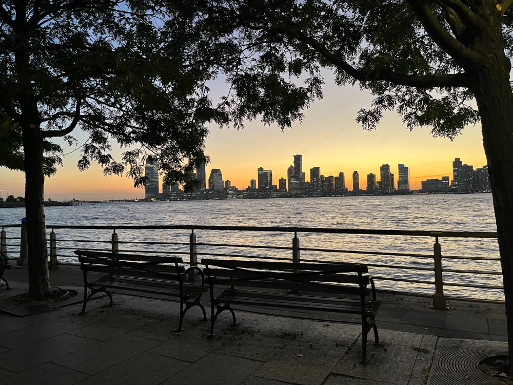 Two empty benches facing a city harbor at sunset 