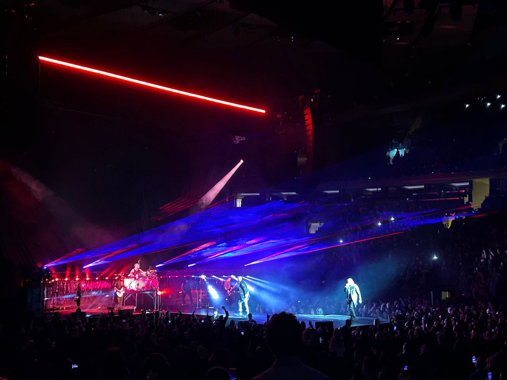 Stage for Three Days Grace. The main stage has red lights with blue lasers lighting up the fog overhead. Both singers are spotlit on the projection coming out from the front of the stage into the crowd.