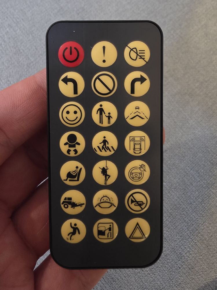 A small remote control with various pictograms of traffic warning signs, a baby, a pregnant person sitting, trumpets prohibited, slippery hallway warning and various other incoherent pictograms