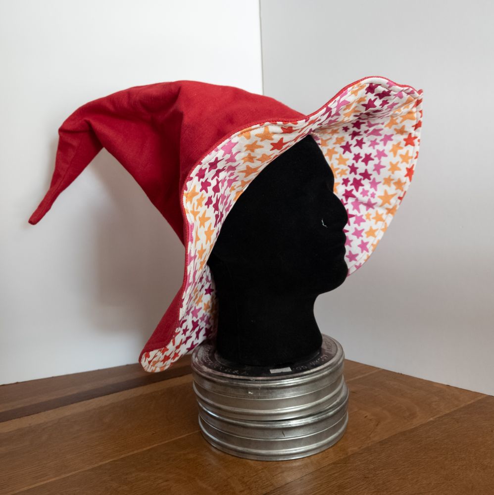 A tall red witch hat on a mannequin head, with a lining that is a pattern of stars in lesbian flag colors