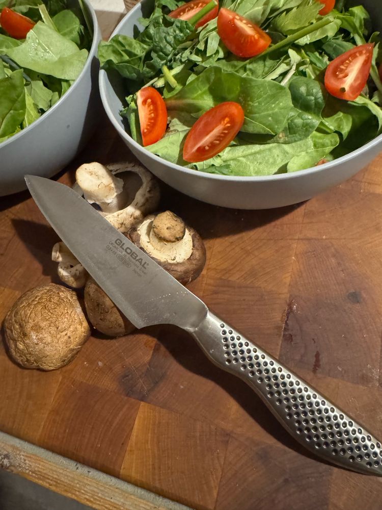 Global knife in front of salad bowls of vegetables and mushrooms. 