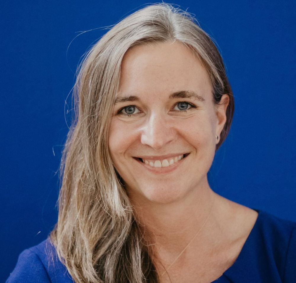 headshot of Zoë Fritz - wearing a dark blue shirt, long blonde hair, smiling.