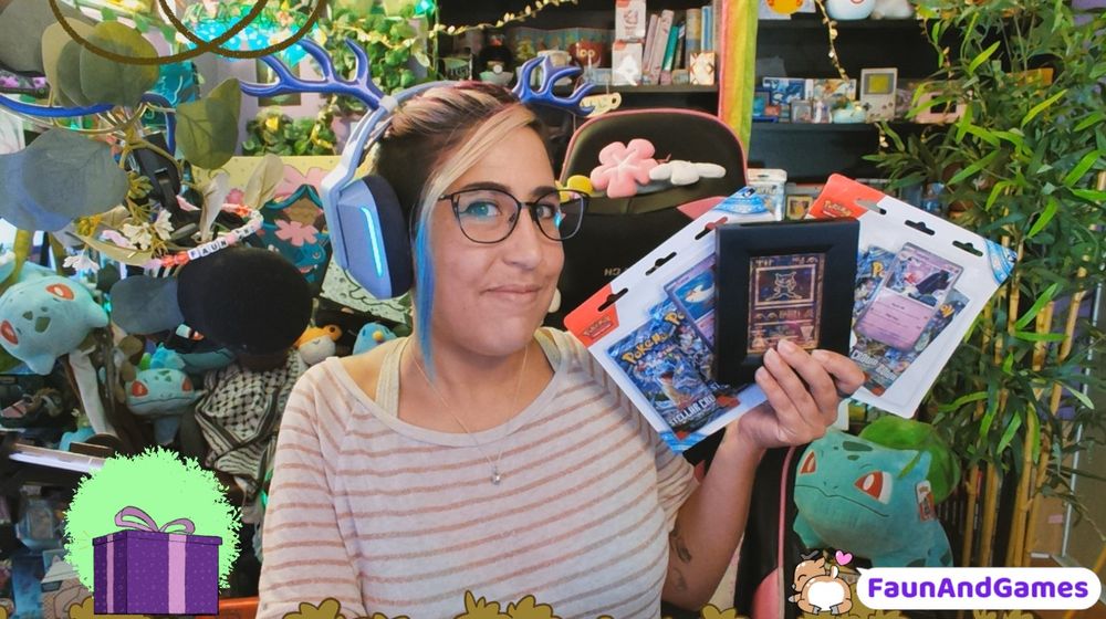 Nonbinary streamer FaunAndGames is smiling at the camera and holding up a stack of Pokemon card packs plus a framed card. FaunAndGames has a tan complexion with a shaved head on one side and a long blue, pink, purple, and white hair tied back.