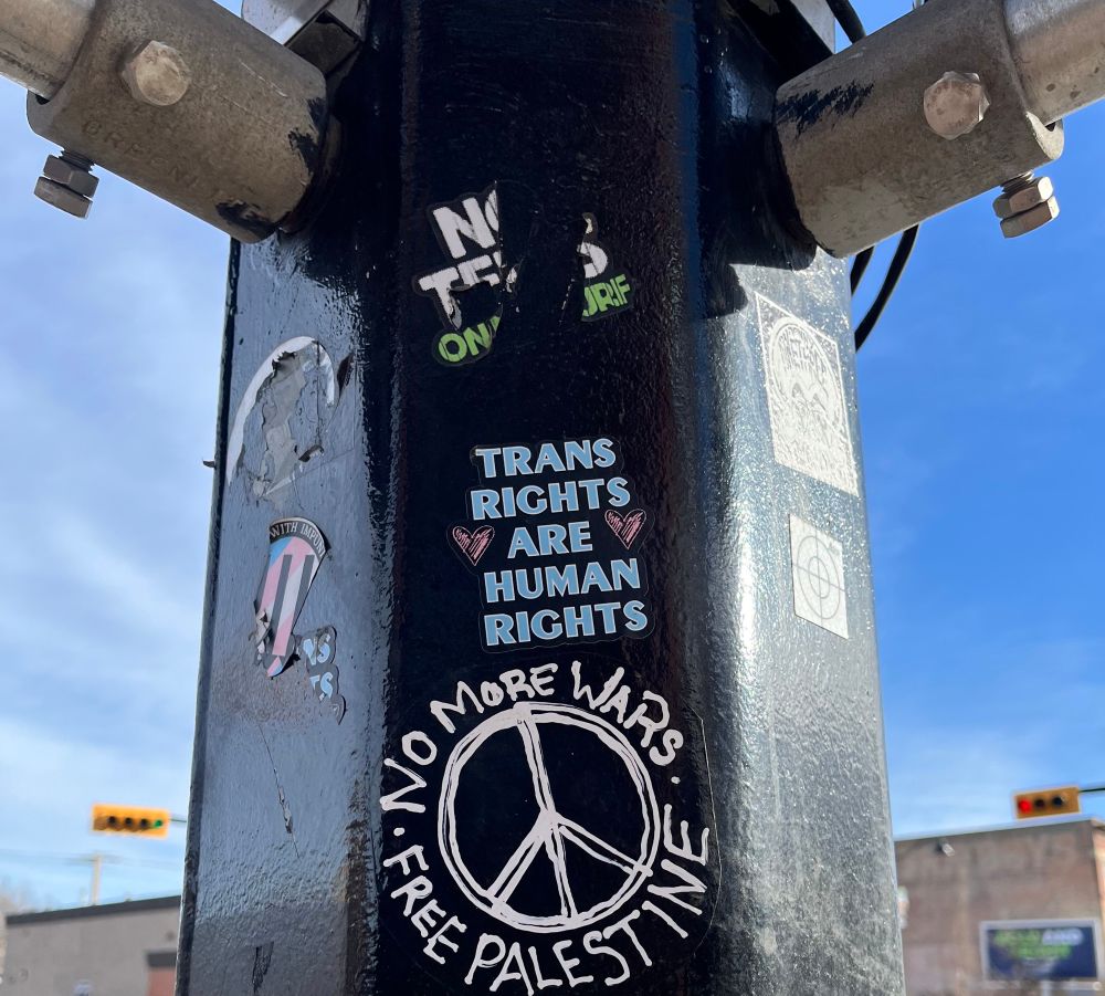 Street pole with Trans rights are human rights. No more wars. Free Palestine stickers.