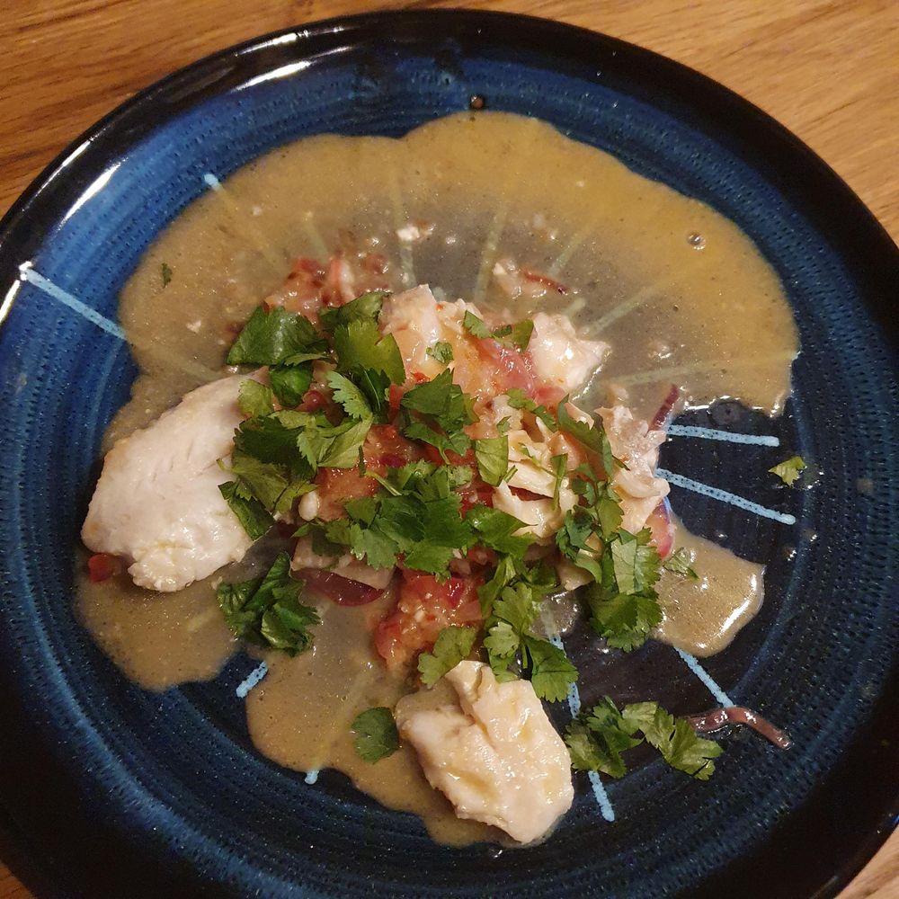Pieces of fish in a white sauce with red onions and chillies, topped with green coriander on a very pretty pottery plate. 
