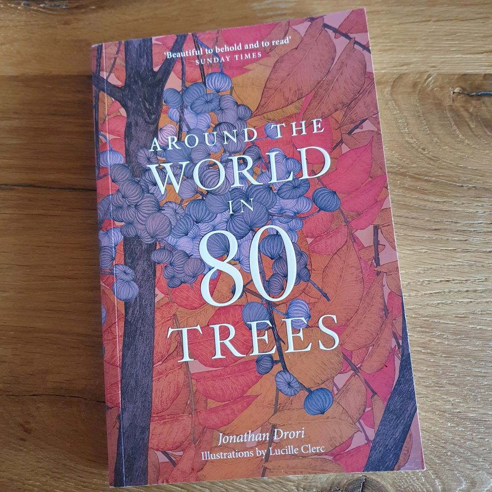 Book on a wooden table: "Around the World in 80 trees" by Jonathan Drori & Lucille Clerk