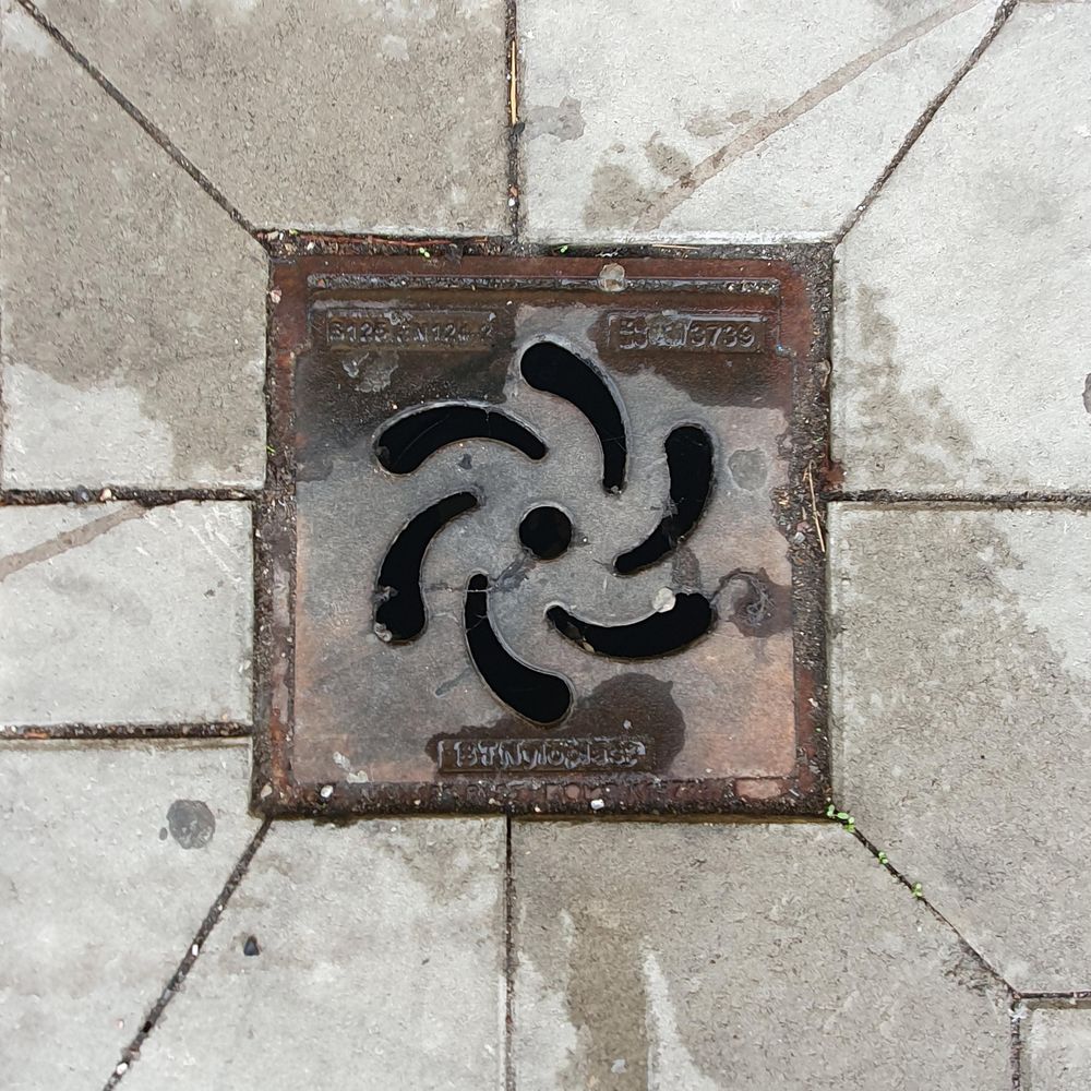 A gully cover with a small round in the middle and comma-like holes around it, making the impression of a spiral. 