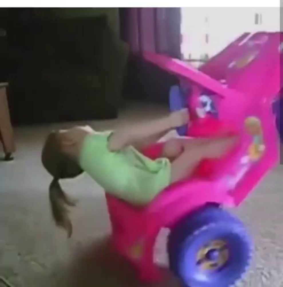 a little girl is laying on her back in a pink toy car