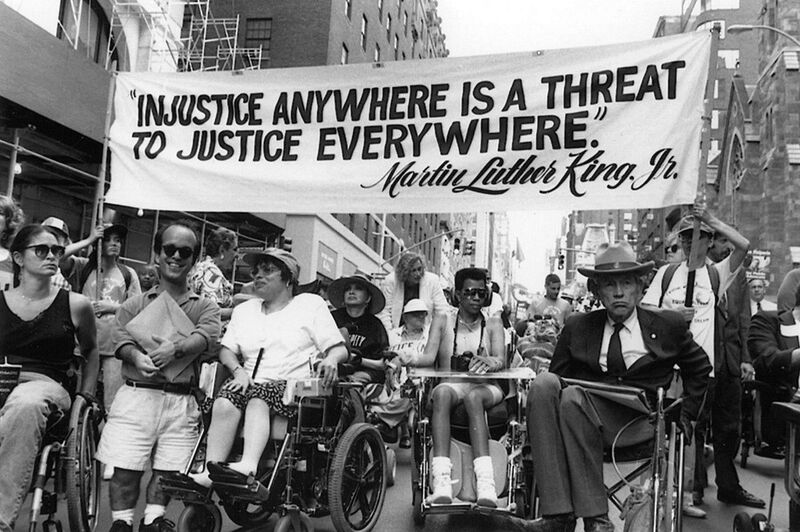 Disability rights advocates including Judy Heumann and Justin Dart under a banner quoting Martin Luther King Jr. “injustice anywhere is a threat to justice everywhere”