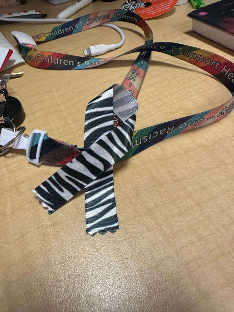 A picture of a badge lanyard sitting on a table with a zebra print awareness ribbon pinned to it.