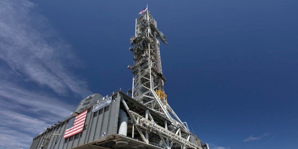 Recortada contra un cielo azul con pocas nubes altas, se ve la plataforma de lanzamiento y su enorme torre de 98 metros de alto, fotografiada desde un punto de vista en el suelo.