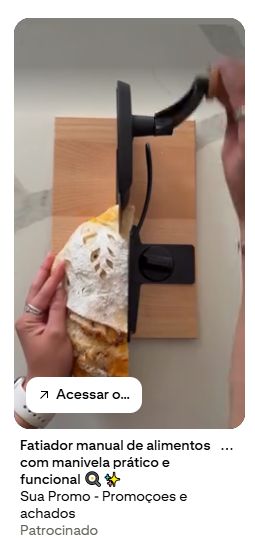 Cortador de pão em madeira e lâmina preta. Funciona com uma manivela. O pão é tipo artesanal, enfarinhado por cima. Quem manipula a máquina é uma pessoa branca, que usa anéis prateados e um relógio branco