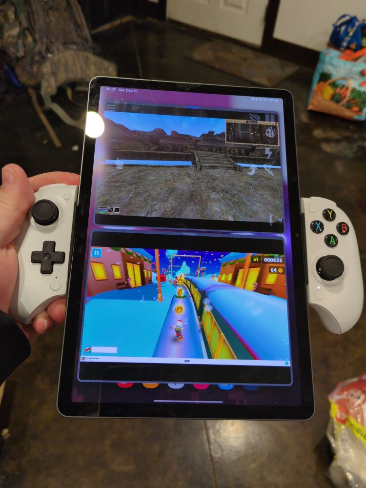 an 11 inch Samsung galaxy tab s9 in vertical orientation with a gamepad attached in the middle where the dpad is on the left of the tablet and the 4 buttons are on the right. the tablet has morrowind open on the top half of the screen and a video of subway surfers on the bottom half