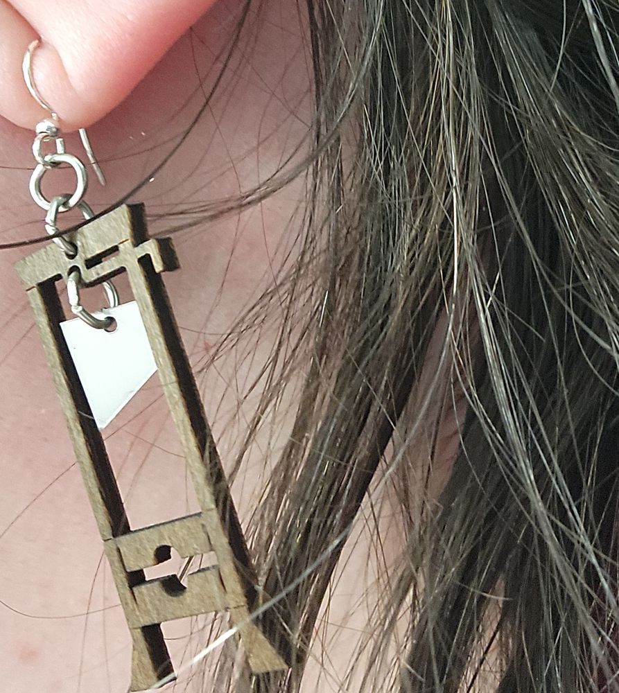 Close up of Christine's ear and long brown hair. Her ear sports a long earring of a guillotine.