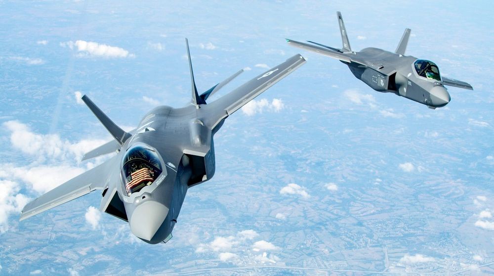 A photo of two US-made F-35 fighter jets flying towards the camera. One has a US flag visible in the cockpit