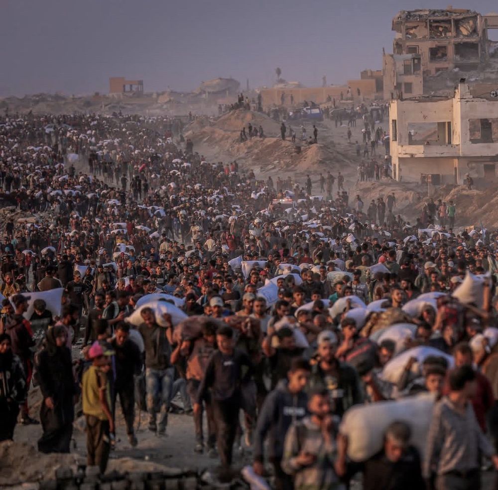Thousands of Palestinians walk along Al-Rasheed Street carrying sacks of flour after aid trucks entered through the Zikim area in northern Gaza. The scene highlights the scale of the humanitarian crisis, as desperate residents rush to secure basic food supplies amid ongoing shortages and siege. Photographer: Saeed Jaras