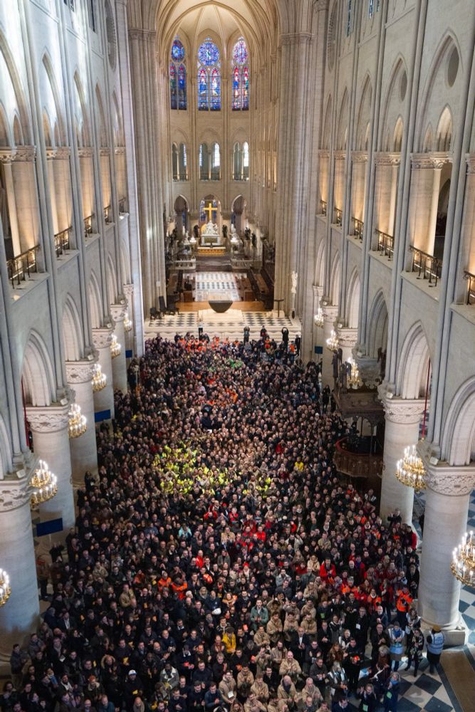 Hundreds of workers, some in high viz vests, cover the floor of Notre Dame cathedral with a photo taken from above, looking down the length of the restored building.