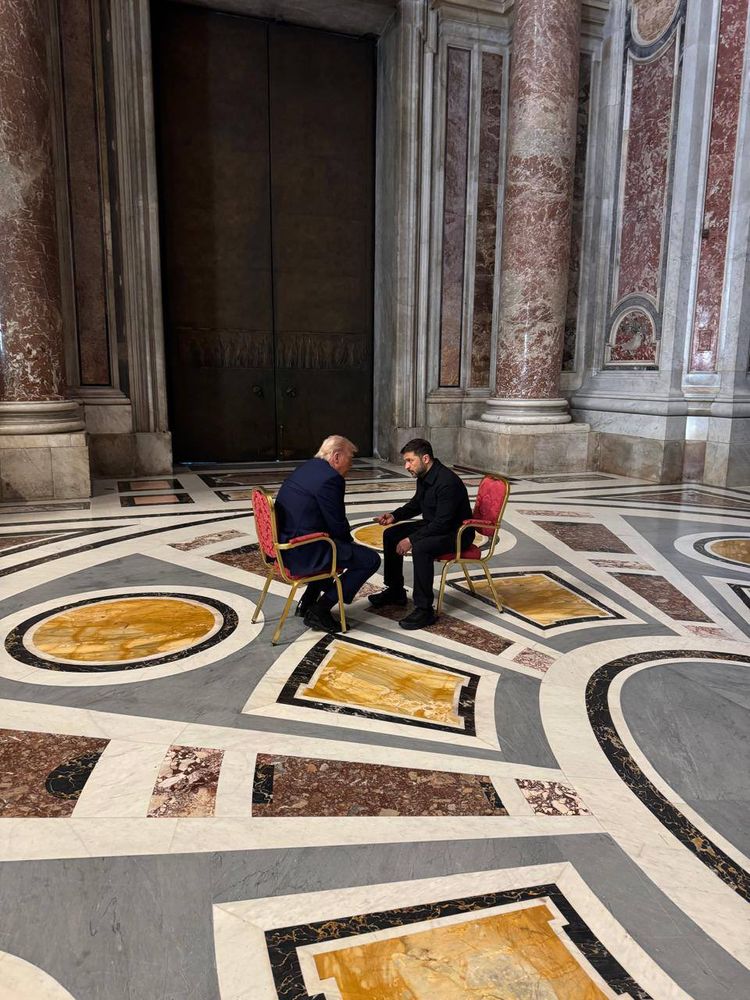 A photo posted by Zelensky’s Presidential office shows Zelensky and Trump alone on the floor of St Peter’s Basillica in the Vatican. They are sat on two red chairs, face to face, inches apart. Zelensky is making a point, fist out. The marble floor and intricate decorations are visible all around.