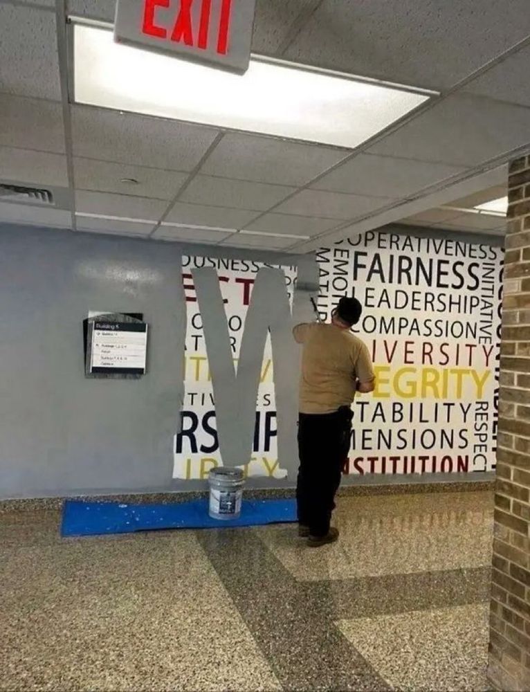 A man is seen painting grey paint to cover up a mural with the words "FAIRNESS, LEADERSHIP, INTEGRITY, COMPASSION and DIVERSITY" in large multicoloured print.