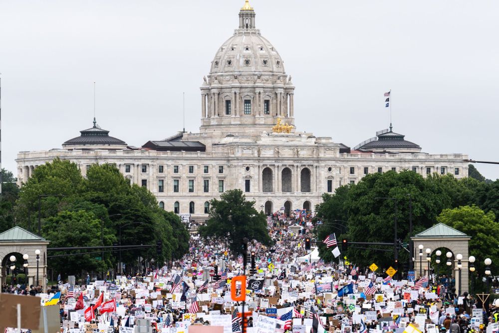 Thousands of people and placards are seen in front of the state capitol. This photo is a credit to Minneapolis photojournalist that goes by the handle Daviss on X