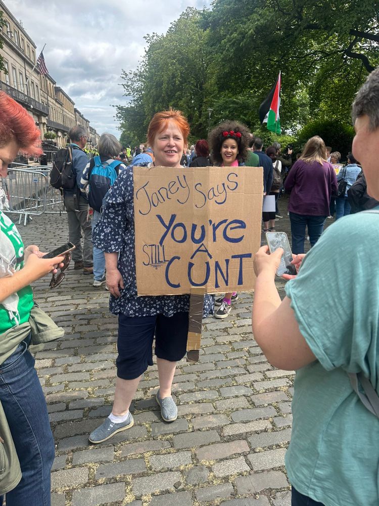 A lady holds a sign aimed at Trump referring to the late Janey Godley which says Janey Says You’re Still a Cunt