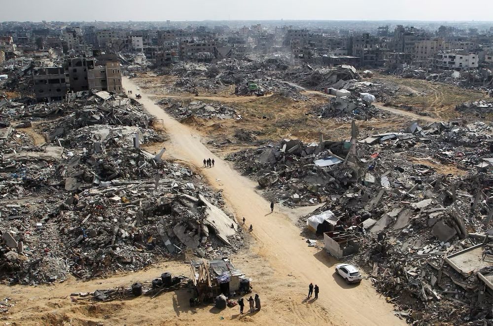 A photo from above showing Palestinians walking past the rubble of buildings destroyed during the Israeli offensive. This photo was taken in February amid a so-called ceasefire between Israel and Hamas. The location is in Rafah in the southern Gaza Strip. Photo credit to: Hatem Khaled of Reuters.