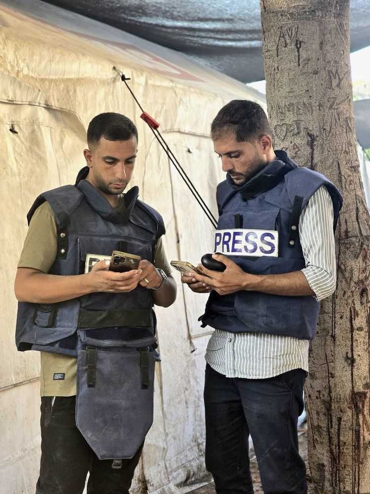A photo of Anas Al-Sharif and his Al Jazeera colleague Mohammad Qrere in their press bullet proof vests looking at their phones. Both are reported killed. Photo credit to Motassem A Dalloul.
