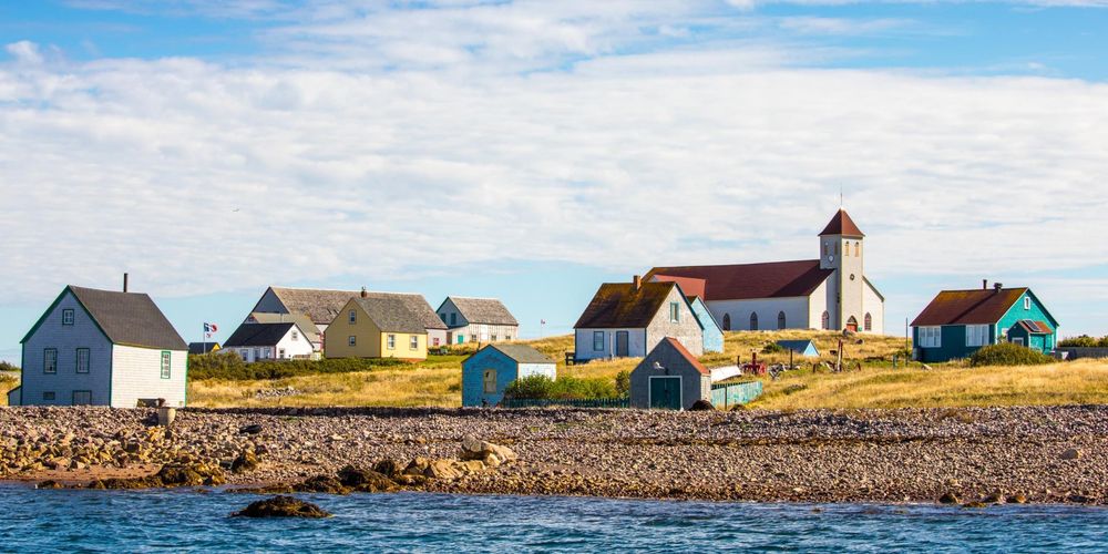 A photo of a few scattered houses and buildings in Saint Pierre and Miquelon along the coastline. It is a French archipelago south of the Canadian island of Newfoundland. Sparsely populated Miquelon-­Langlade island contains the Grand Barachois lagoon, home to seabirds and seals. An island nearby, Île-aux-Marins, features an abandoned fishing village.