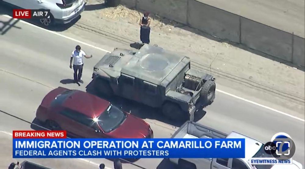 A protestor in white t shirt is seen gesturing toward a Humvee gesturing for it to stop