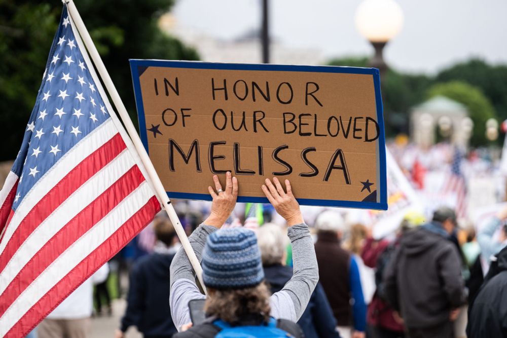 A woman protestor holds up a sign that reads “In honor of our beloved Melissa”
