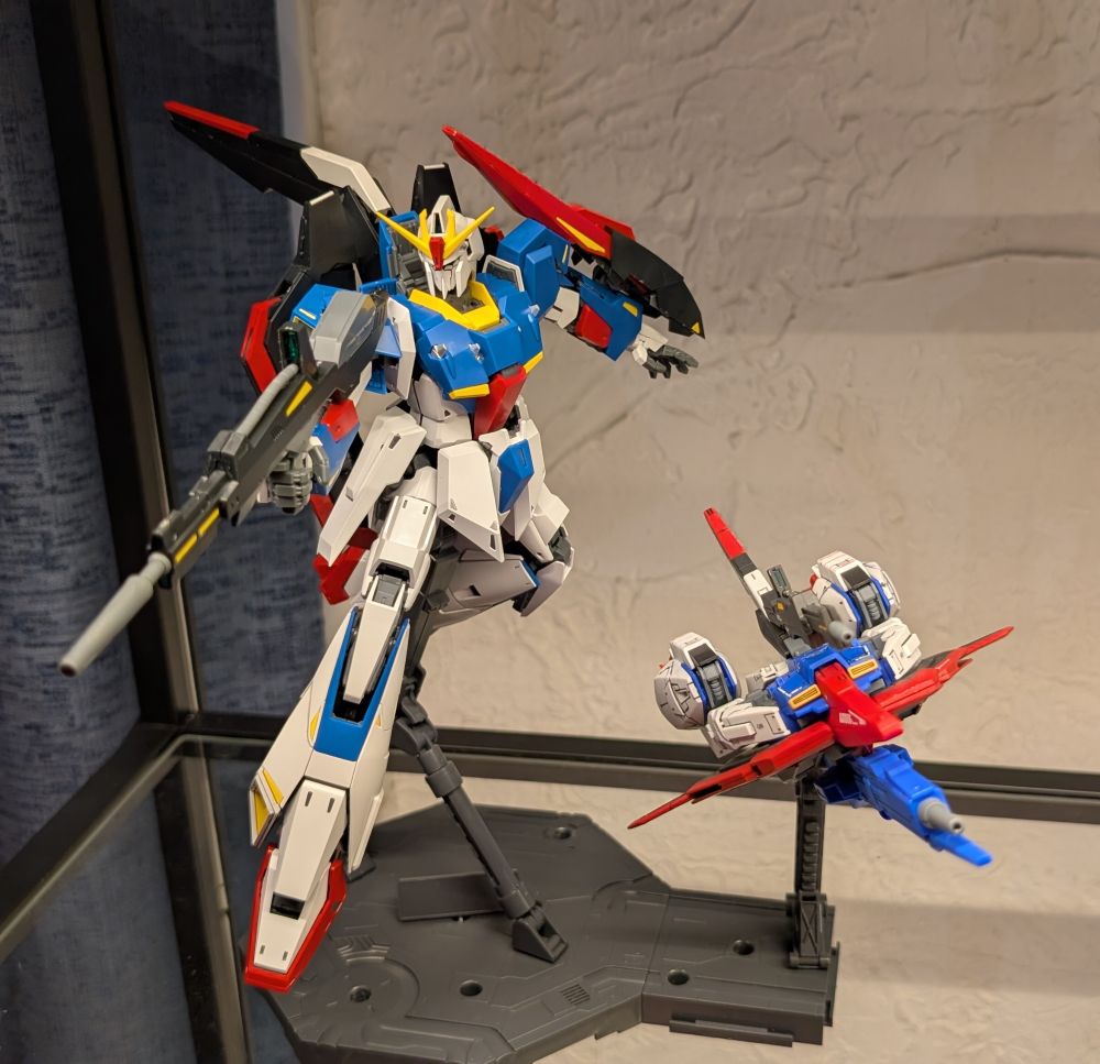 A display of two model kits, one in robotic mobile suit form, the other one in its flight mode. The larger of the two is the Zeta Gundam, a red, white and blue mobile suit from the 1985 anime series. Mobile Suit Zeta Gundam. It is 1/100 scale And is posed holding its gun as if to fire with one leg outstretched and the other tucked behind it as though flying through space. 

The smaller of the two models is the Zeta Gundam in its Wave Rider flight mode. It looks a bit like a jet fighter, and is posed as though zooming along to the side of its alternate form.