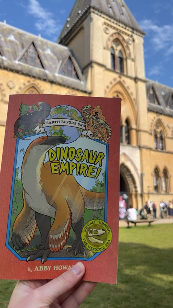 Photo of hand holding up dinosaur empire! By Abby Howard. The person behind the camera is sat in the shade in front of the museum of natural history in Oxford.